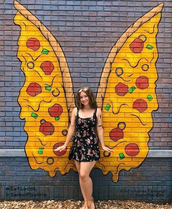 a woman standing in front of a brick wall with a butterfly painted on it's side