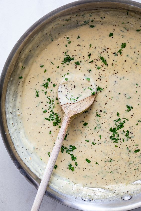 a wooden spoon in a pot filled with broccoli and cheese sauce on top of a table