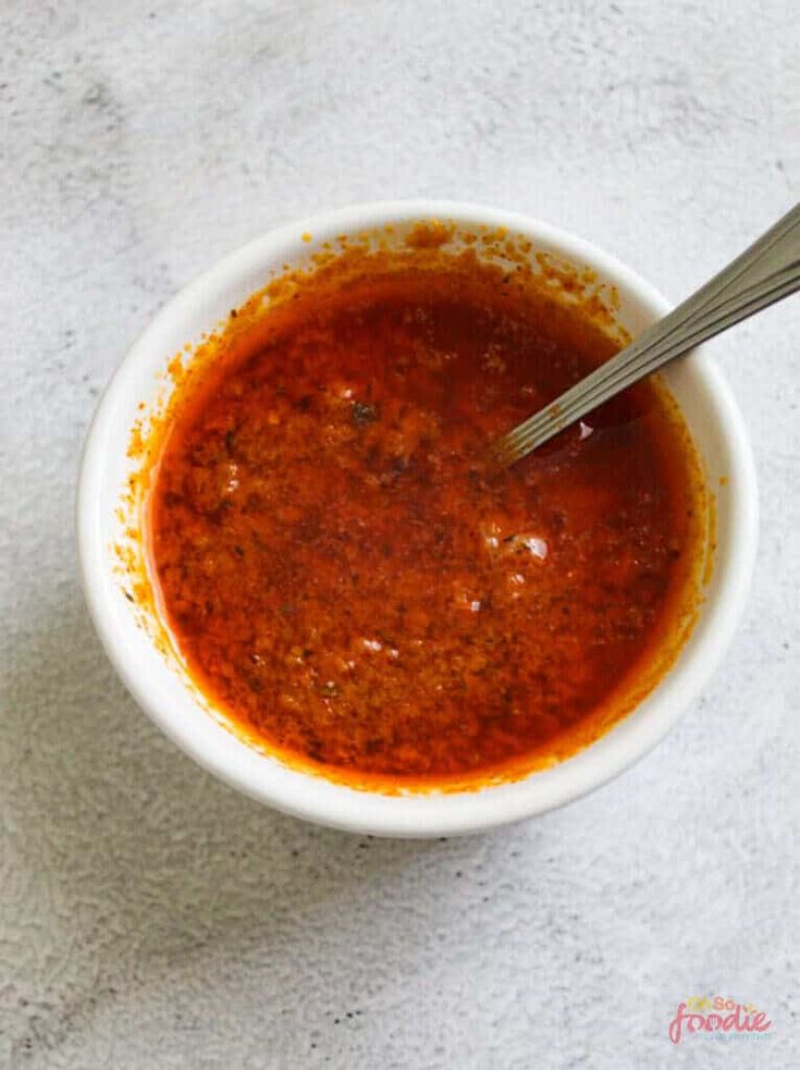 a white bowl filled with red sauce on top of a table next to a spoon