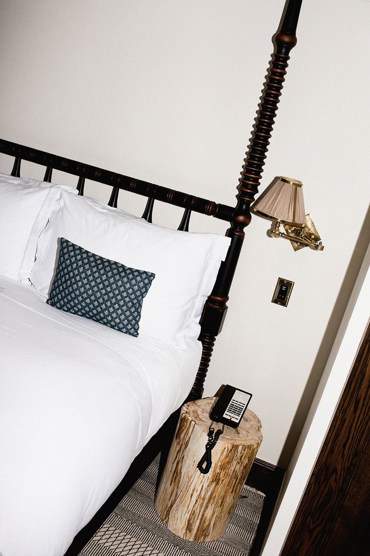 a bed with white sheets and pillows next to a night stand on a rug in a bedroom