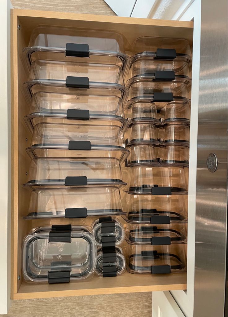 an organized kitchen drawer filled with clear plastic containers and black lids for food prepping