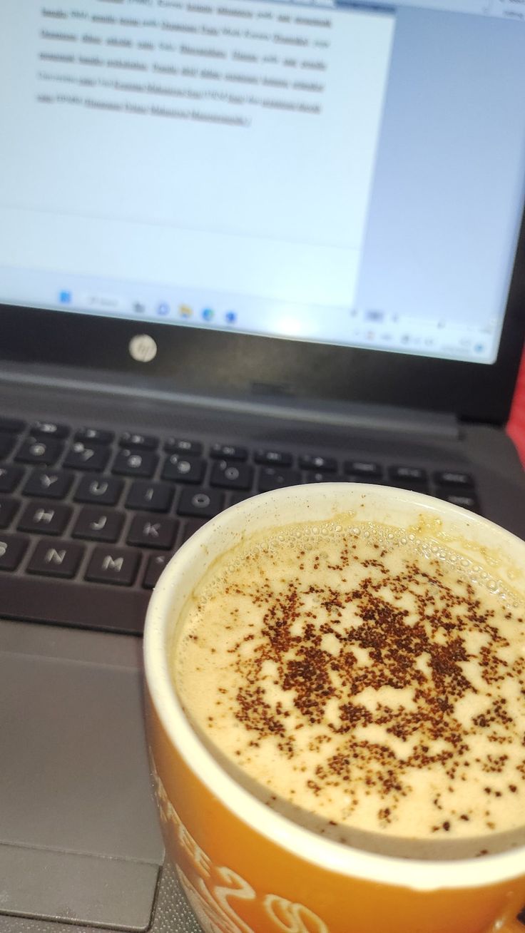 a cup of coffee sitting in front of a laptop computer