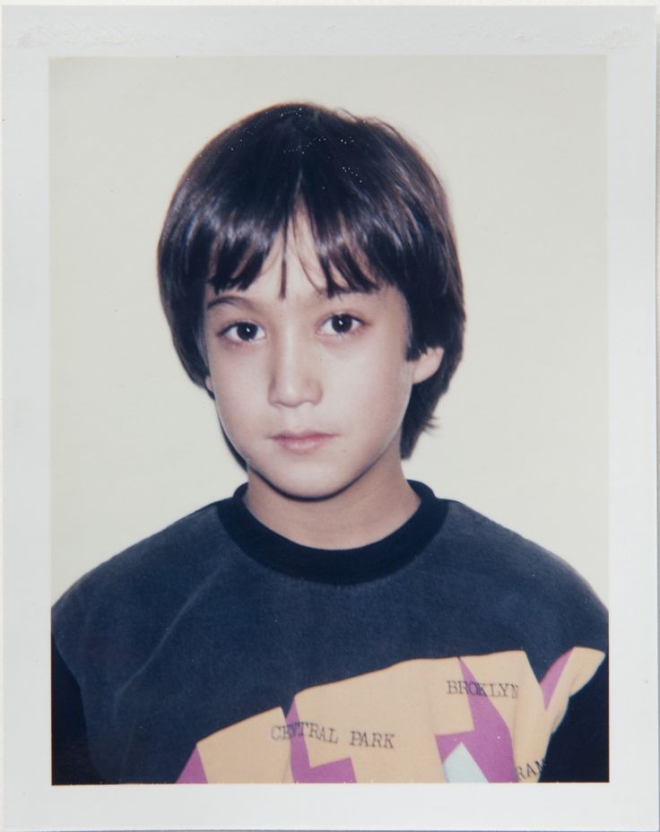 an old photo of a young boy wearing a t - shirt and looking at the camera