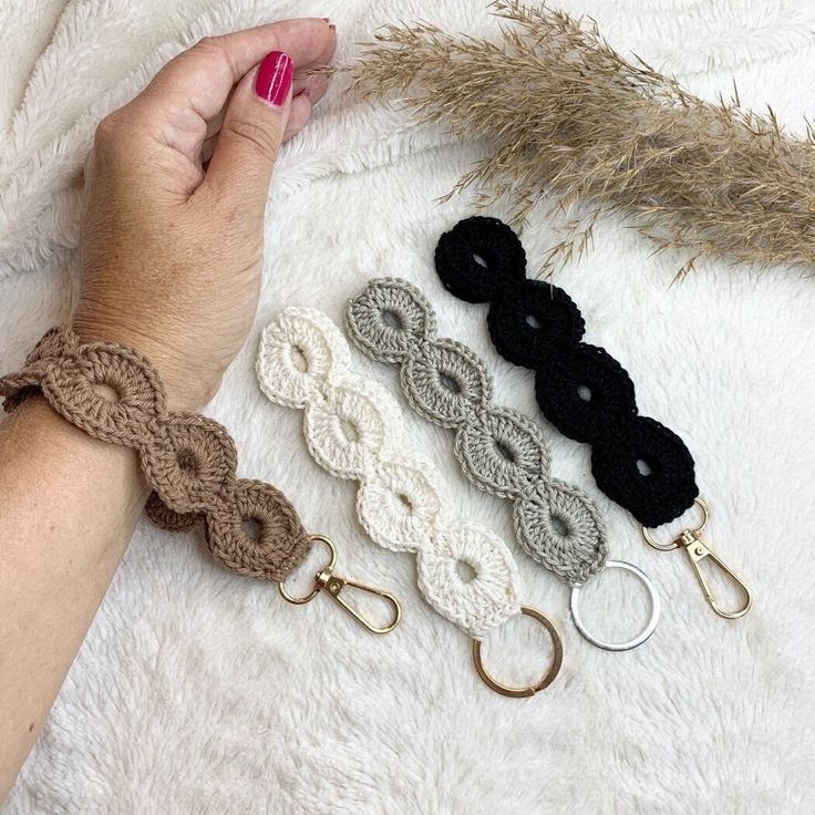 the woman is holding her hand near four crocheted bracelets on a white blanket