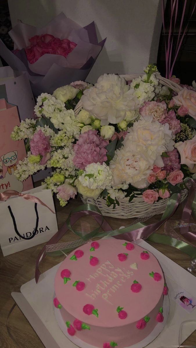 a pink cake sitting on top of a table next to flowers and greeting cards with the words happy birthday