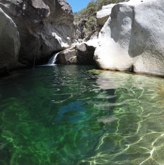 the water is crystal green and clear in this pool at the base of a mountain