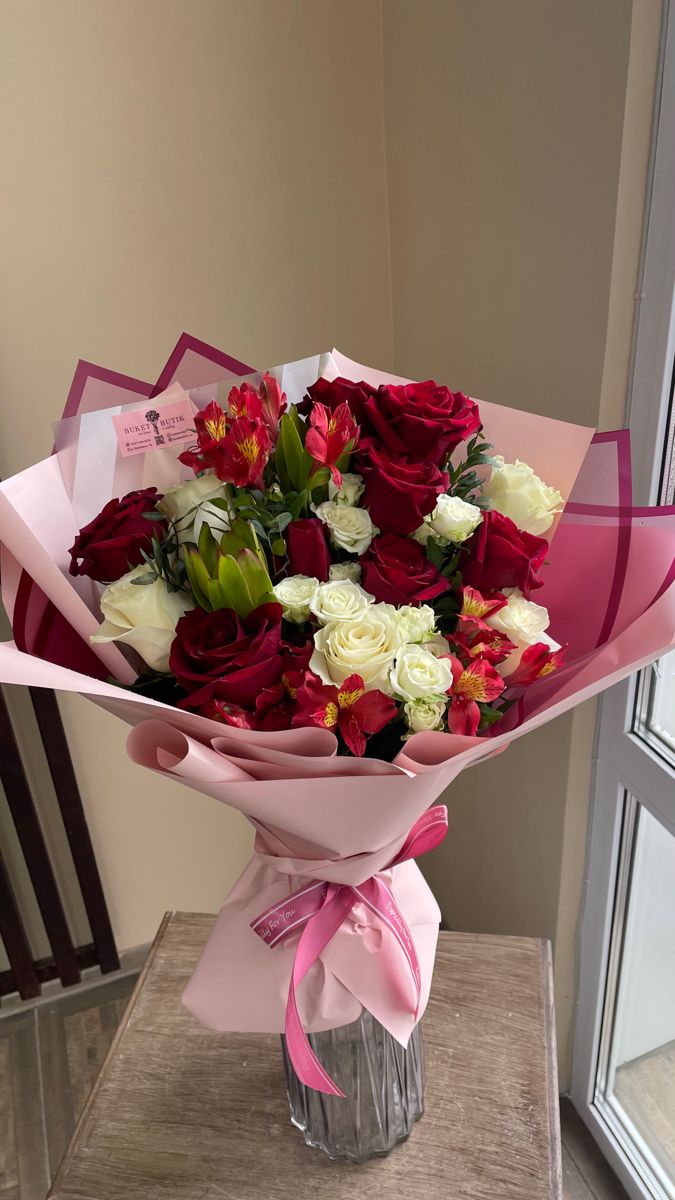 a bouquet of red and white flowers sitting on top of a table next to a window