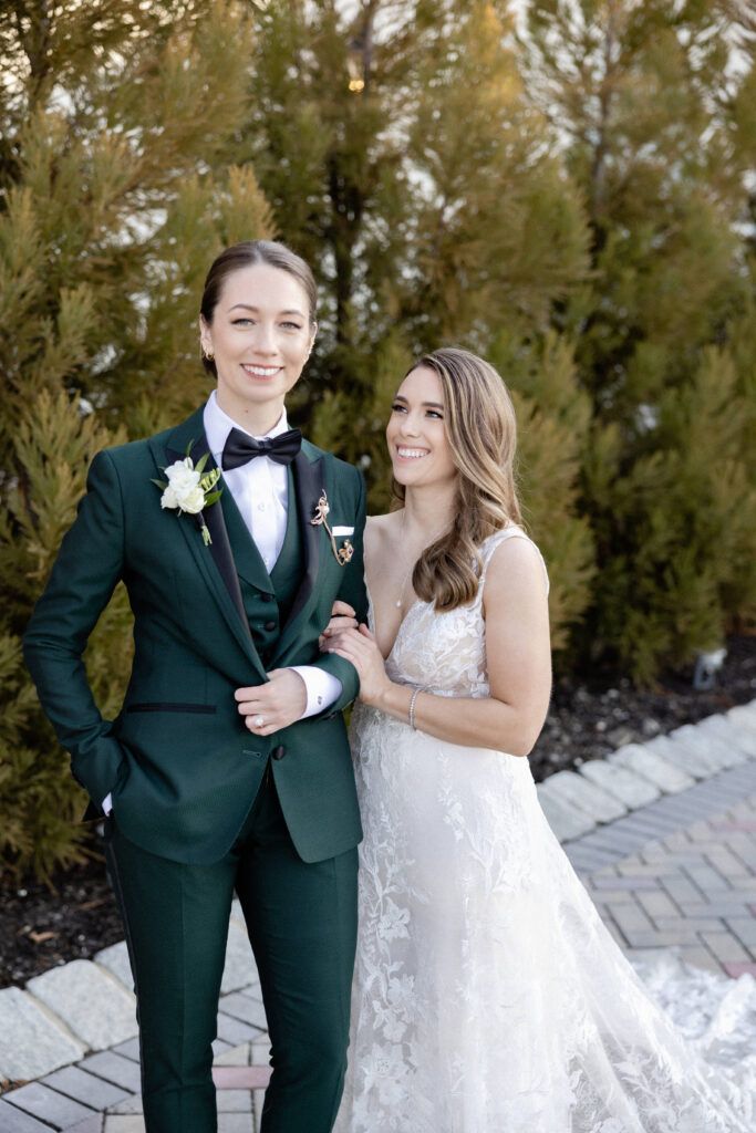 a bride and groom standing next to each other in front of some bushes wearing green tuxedos