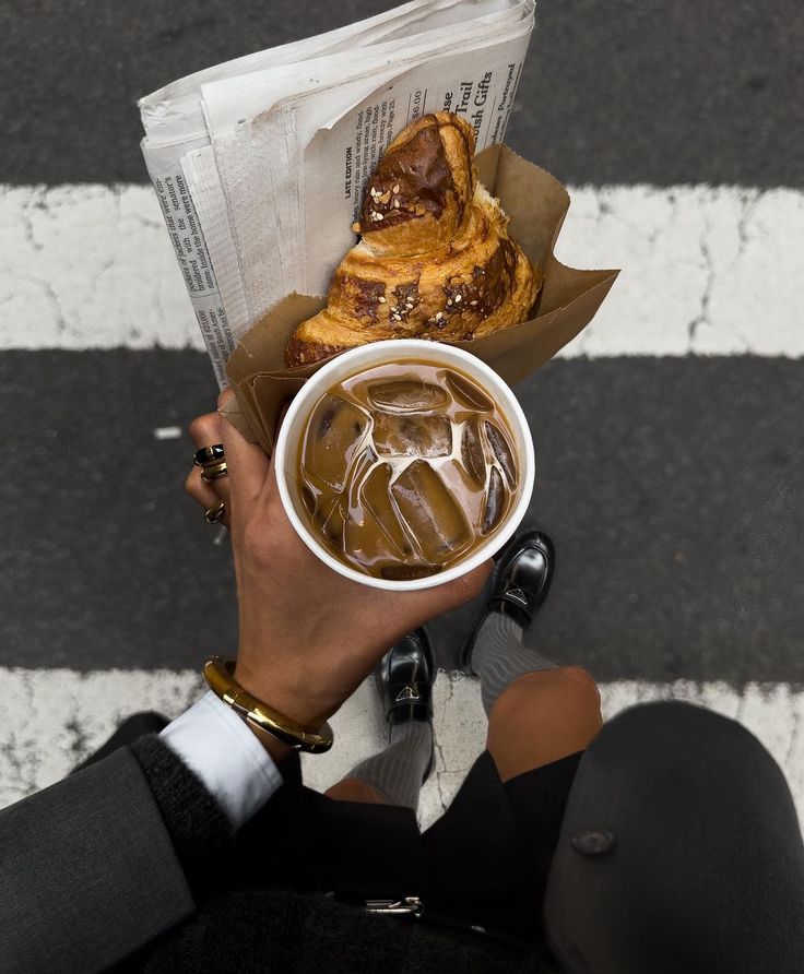 a person holding a cup of coffee and some pastries in their hands on the street