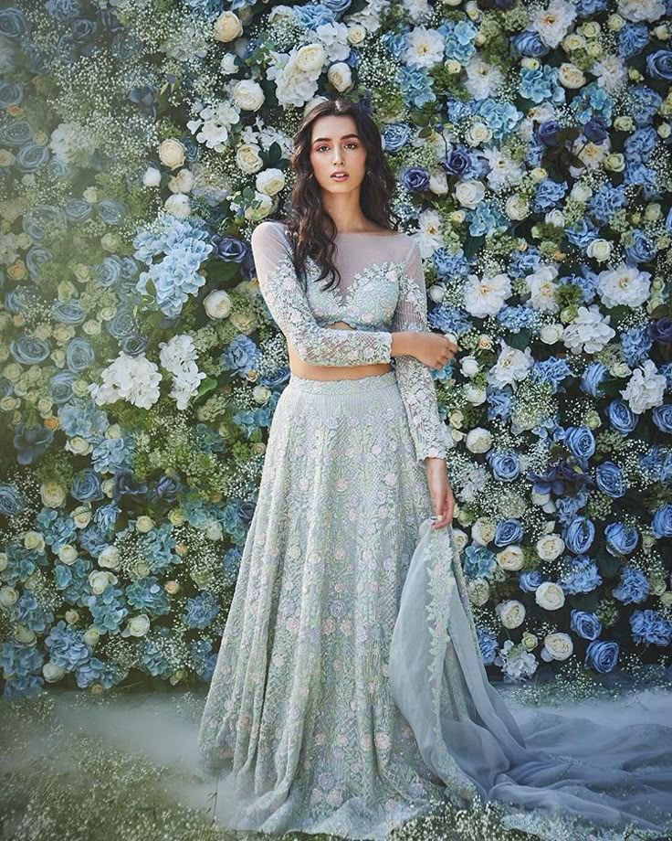 a woman standing in front of flowers wearing a white and blue dress with long sleeves