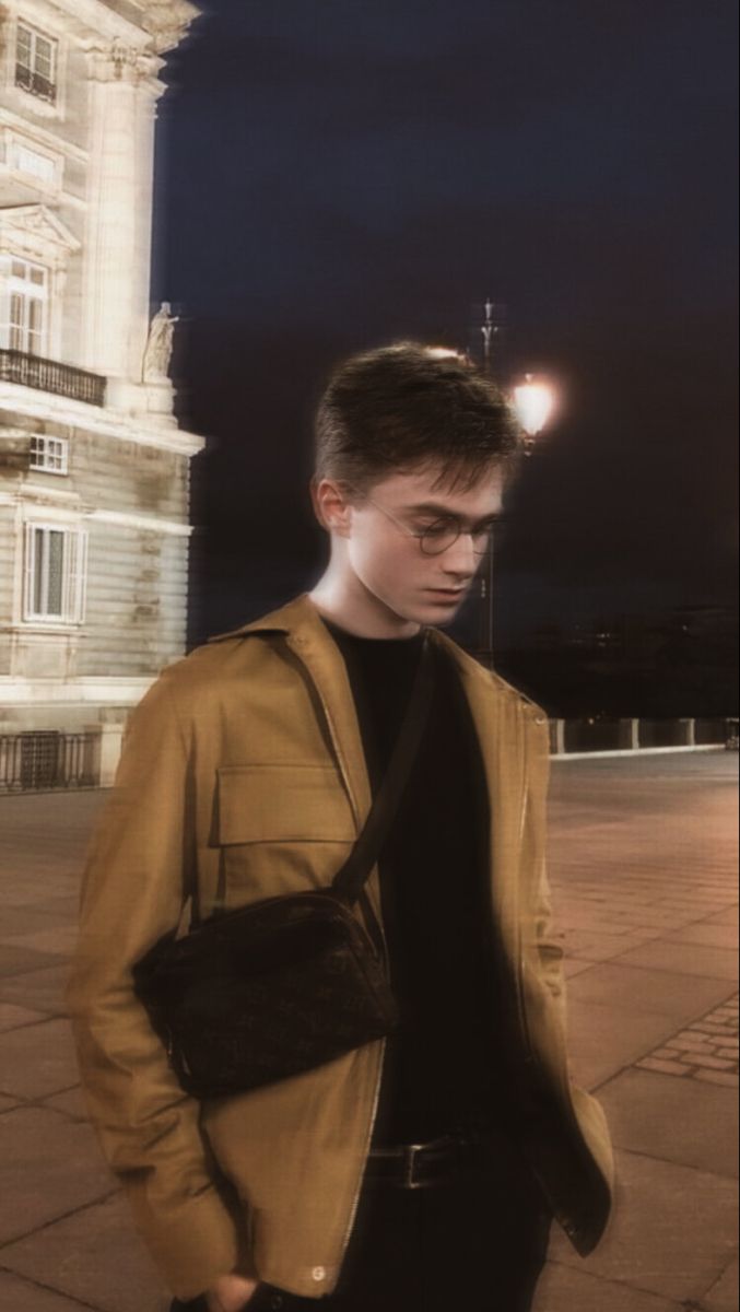 a young man standing in front of a building at night with his hand on his hip