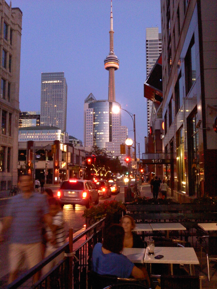 people are sitting at tables in an outdoor cafe with the cn tower in the background