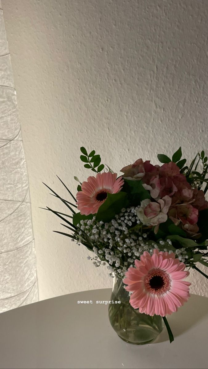 a vase filled with pink flowers sitting on top of a white table next to a wall