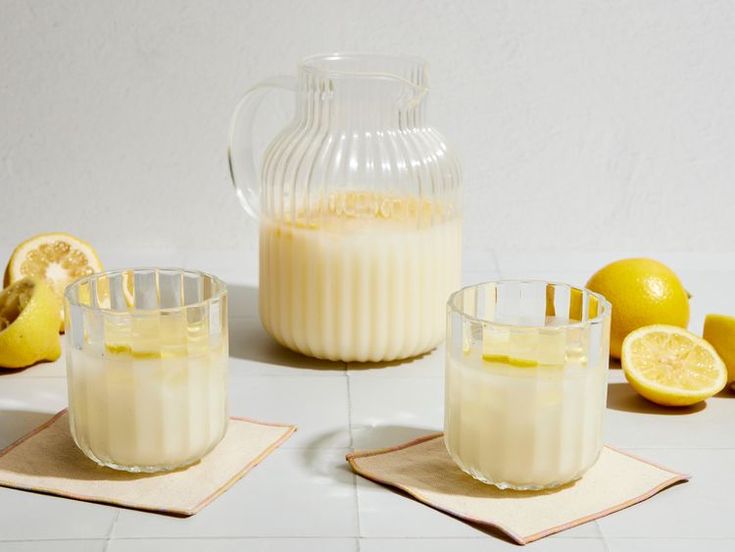 there are three glasses and one pitcher on the table with lemons around it,