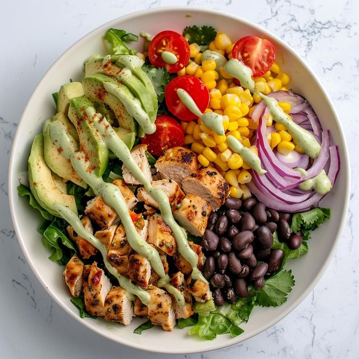 a salad with chicken, avocado, tomatoes, black beans, and dressing