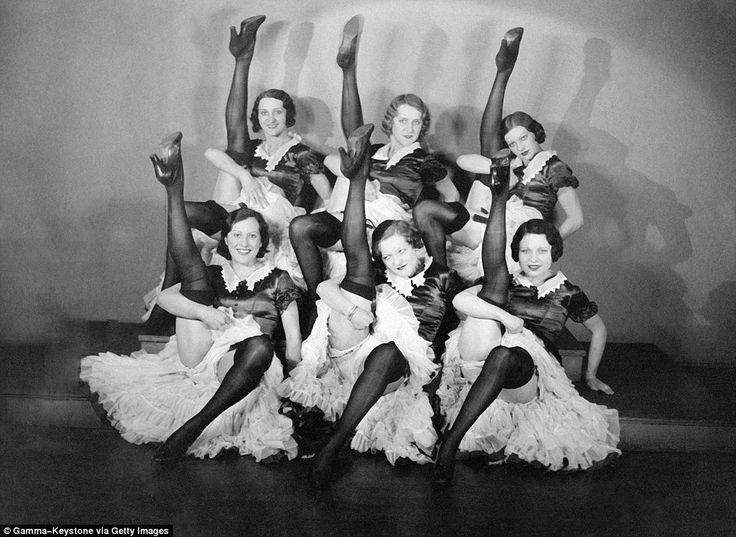 an old black and white photo of women in costumes posing for a group shot with their legs up