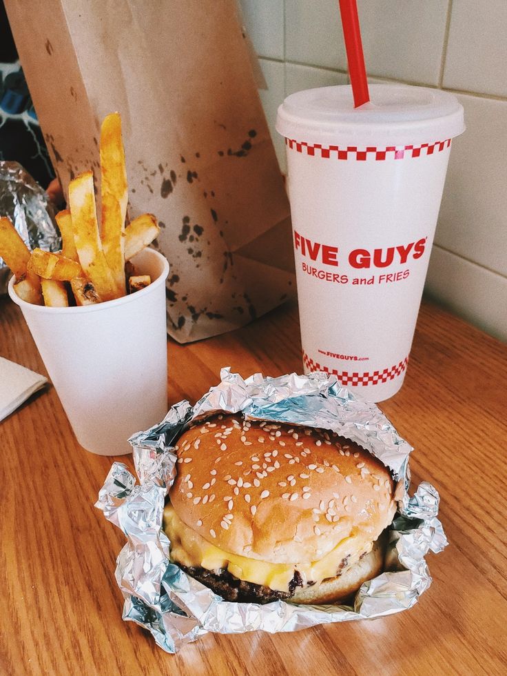 a burger and fries are on the table next to a cup of soda, which is sitting beside it