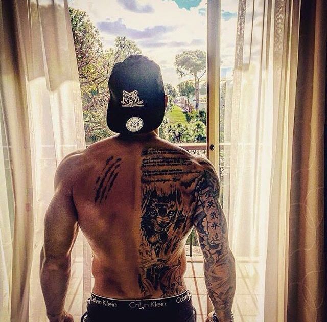 a man with tattoos on his back standing in front of a window