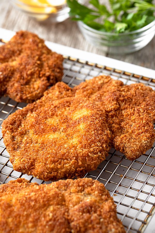 three fried chicken patties cooling on a wire rack next to lemons and greens