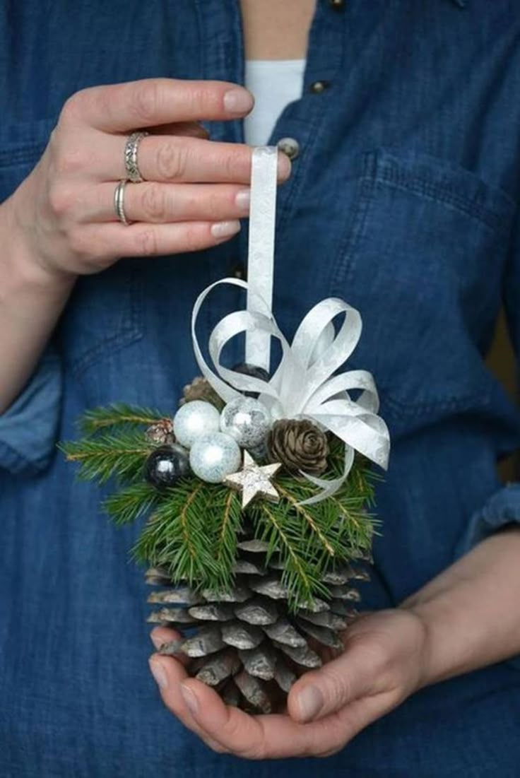 a person holding a pine cone in their hands with christmas decorations on it and snow falling around them