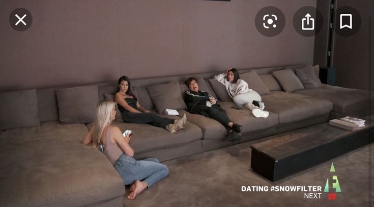 four people sitting on couches in a living room with one person holding a cell phone