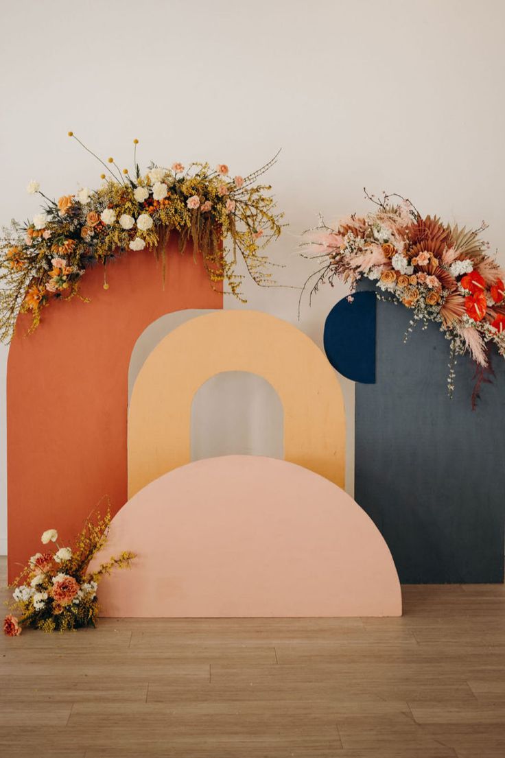 three different colored vases with flowers on them sitting in front of a white wall