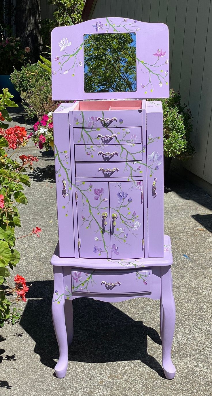 a purple dresser with flowers painted on the drawers and mirror in it's drawer