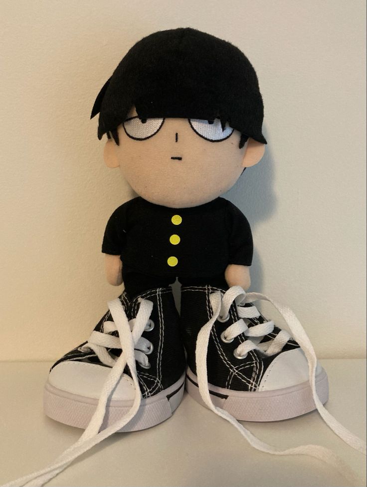 a black and white stuffed toy with glasses on it's head sitting next to a pair of shoes