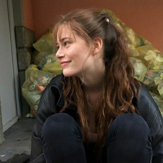 a woman sitting on the ground next to a pile of bags and looking off into the distance