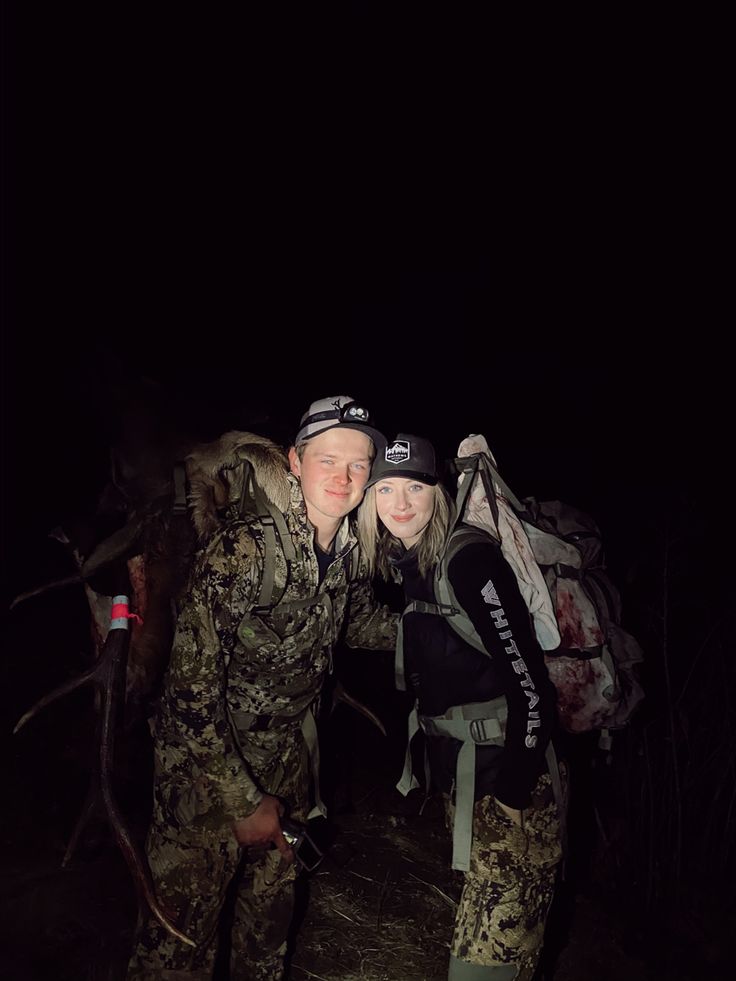 a man and woman standing next to each other with backpacks on their backs in the dark