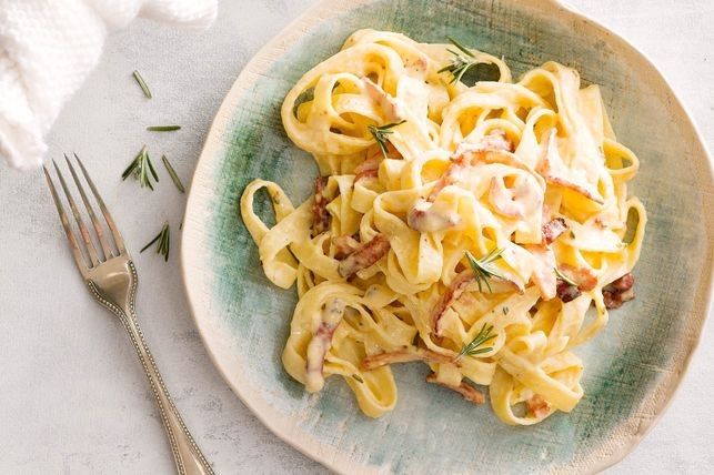 a plate of pasta with meat and cream sauce on it next to a silver fork