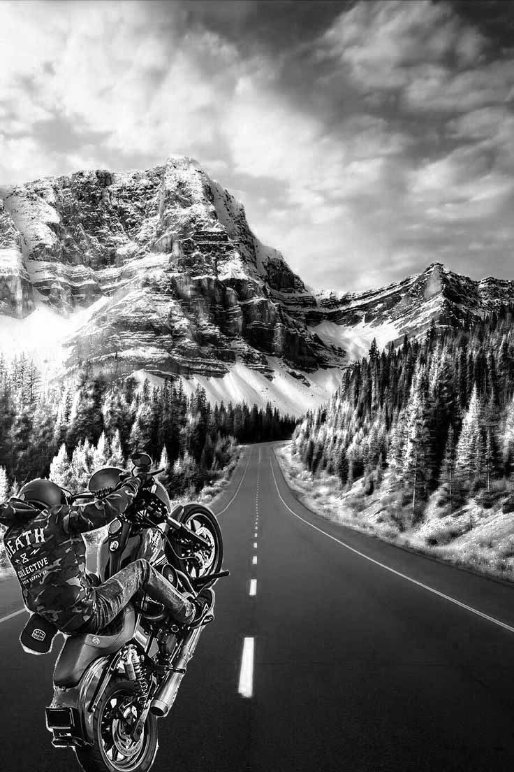 a black and white photo of a motorcyclist riding down the road with mountains in the background