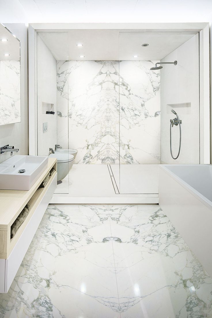 a white bathroom with marble flooring and wall to wall glass shower stall, double sinks, and separate bathtub