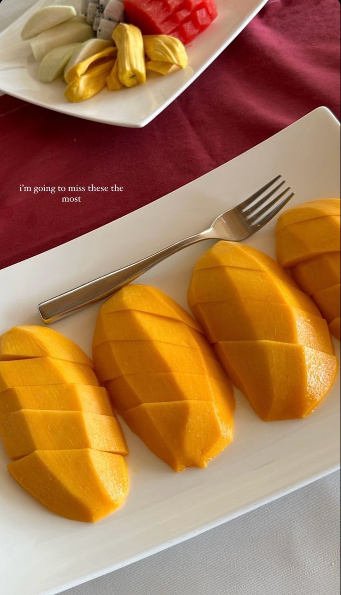 four pieces of mango on a white plate with a fork and knife next to it