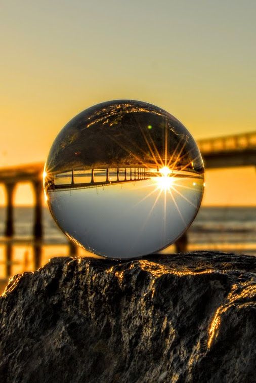 a glass ball sitting on top of a rock next to the ocean with a bridge in the background