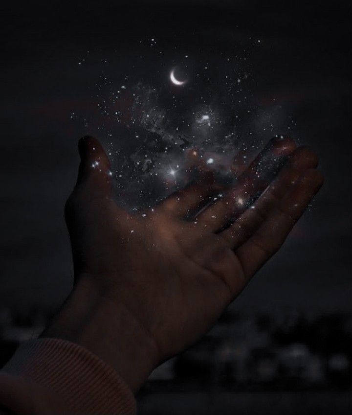 a person holding out their hand to the stars in the night sky with city lights behind them