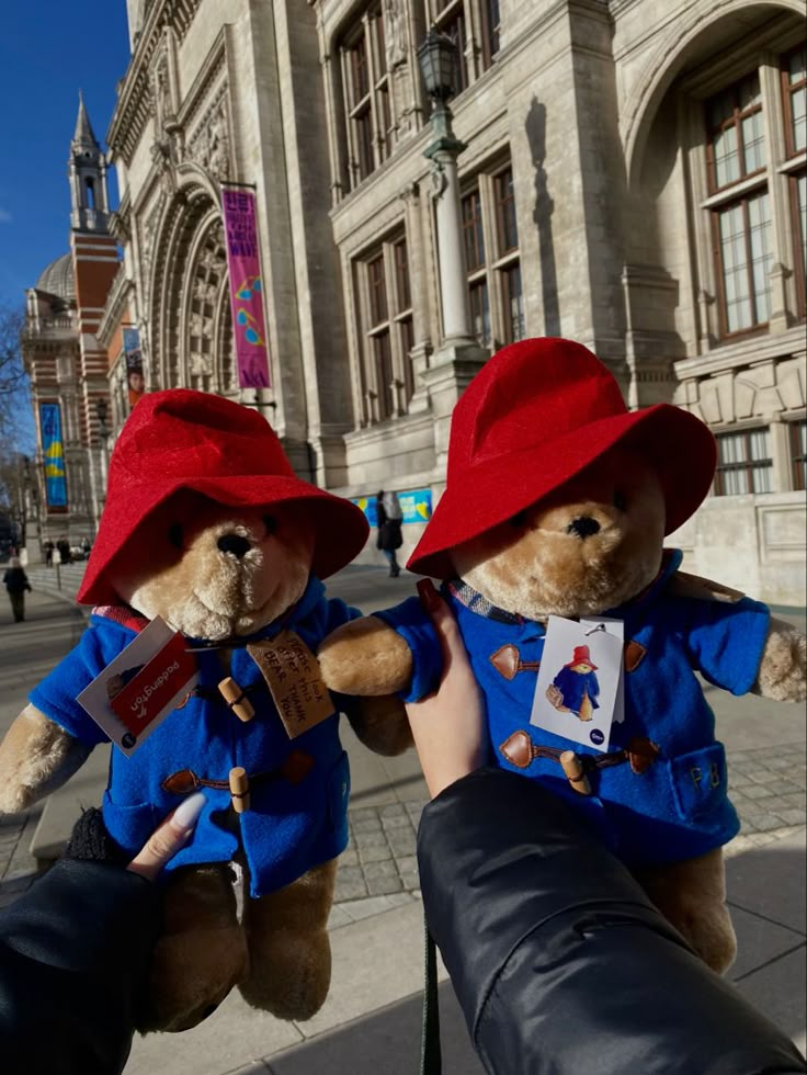 two teddy bears dressed in red hats and blue shirts are being held by someone's hand