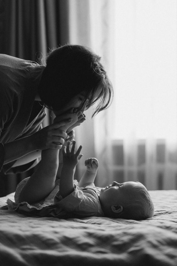 a woman kisses her baby while laying on the bed with it's foot up