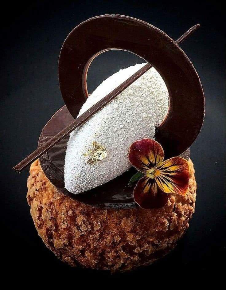 a piece of chocolate cake sitting on top of a wooden table next to a flower