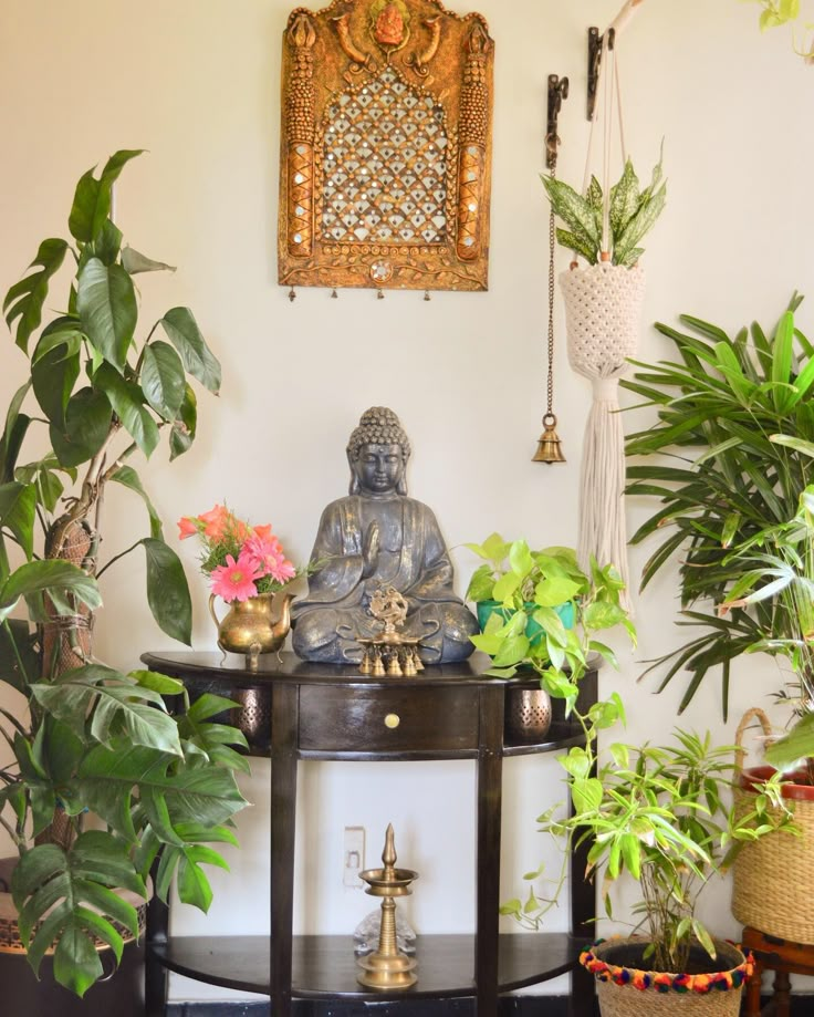 a buddha statue sitting on top of a wooden table surrounded by potted plants and greenery