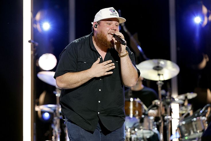 a man singing into a microphone while standing in front of drummers and drums on stage