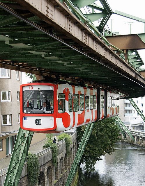 a red and white train traveling over a bridge next to a body of water with buildings in the background