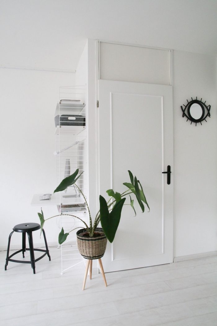 a houseplant in a basket next to a white door with a black clock on the wall