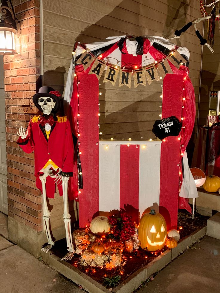 a halloween display with skeletons and pumpkins in front of a red striped tent that says arney