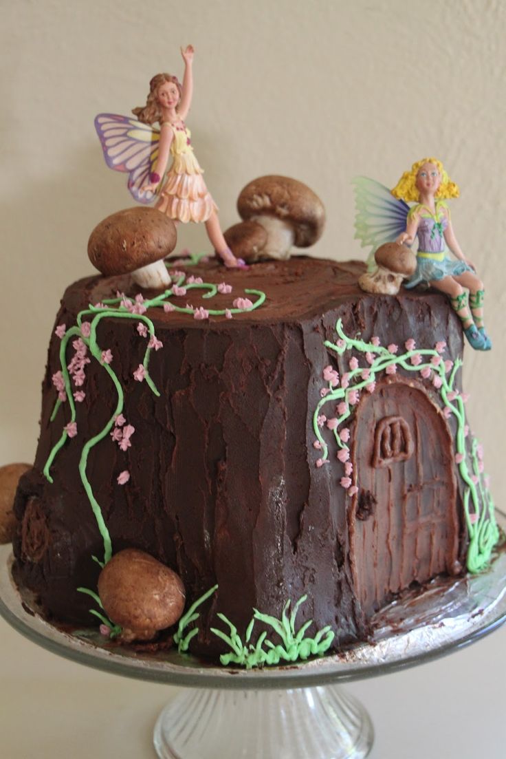 a chocolate cake decorated with fairy figurines and mushrooms on top, sitting on a pedestal