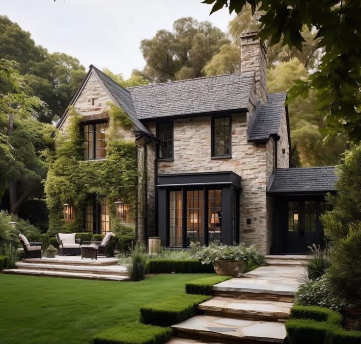 a stone house with steps leading up to the front door and lawn in front of it