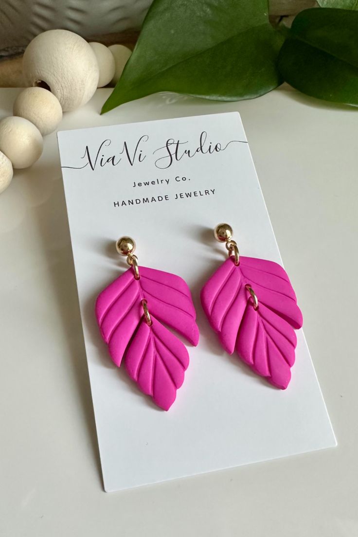 the pink earrings are on display next to a card with an image of a plant