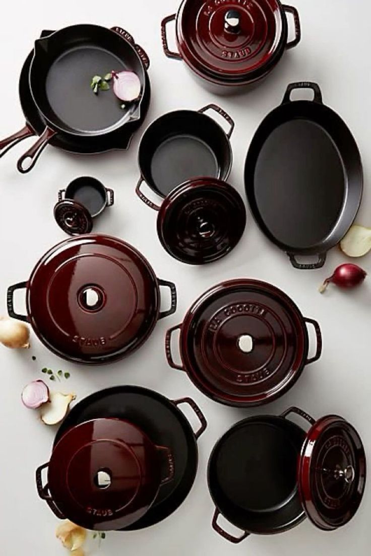 many pots and pans are arranged on a white surface with red onions around them