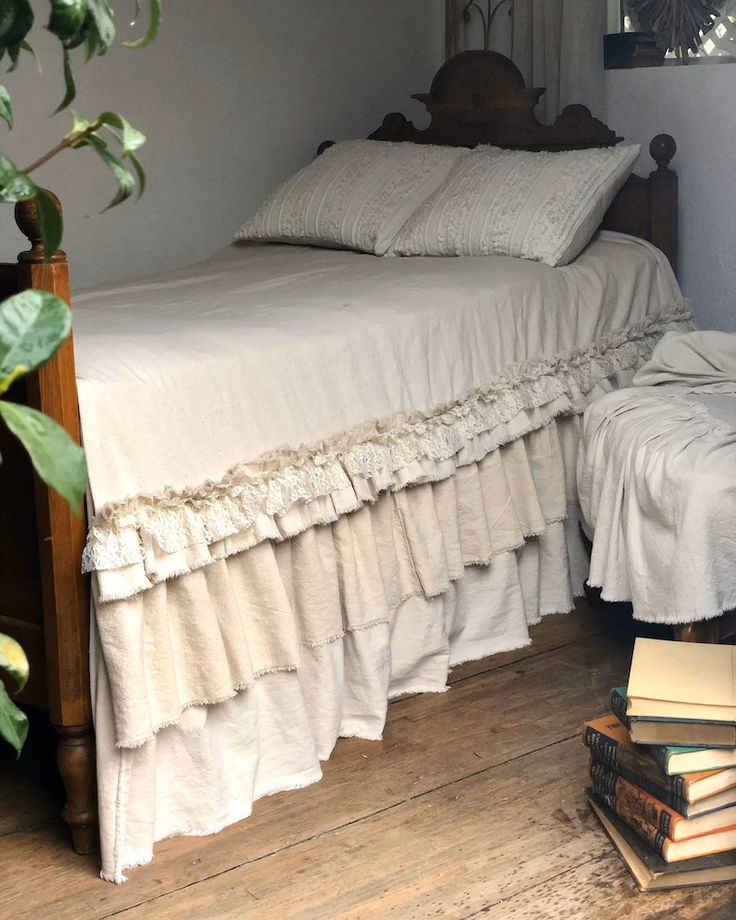 a bed sitting next to a pile of books on top of a wooden floor