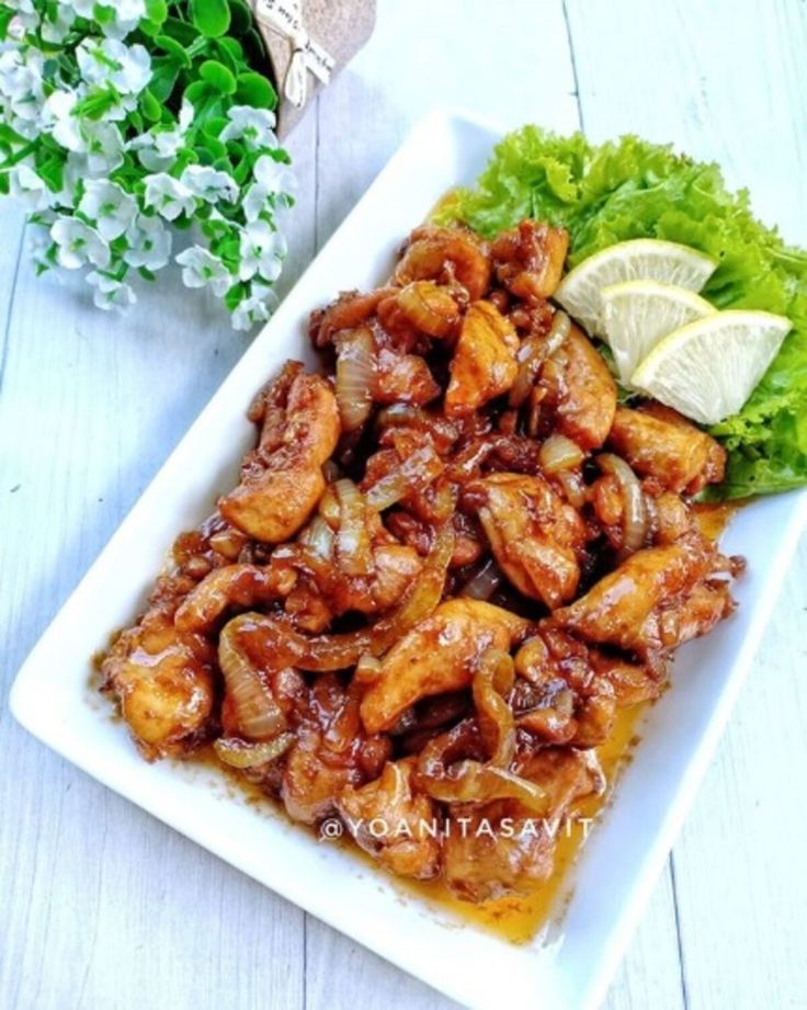 chicken wings with sauce and lettuce on a white plate next to a plant